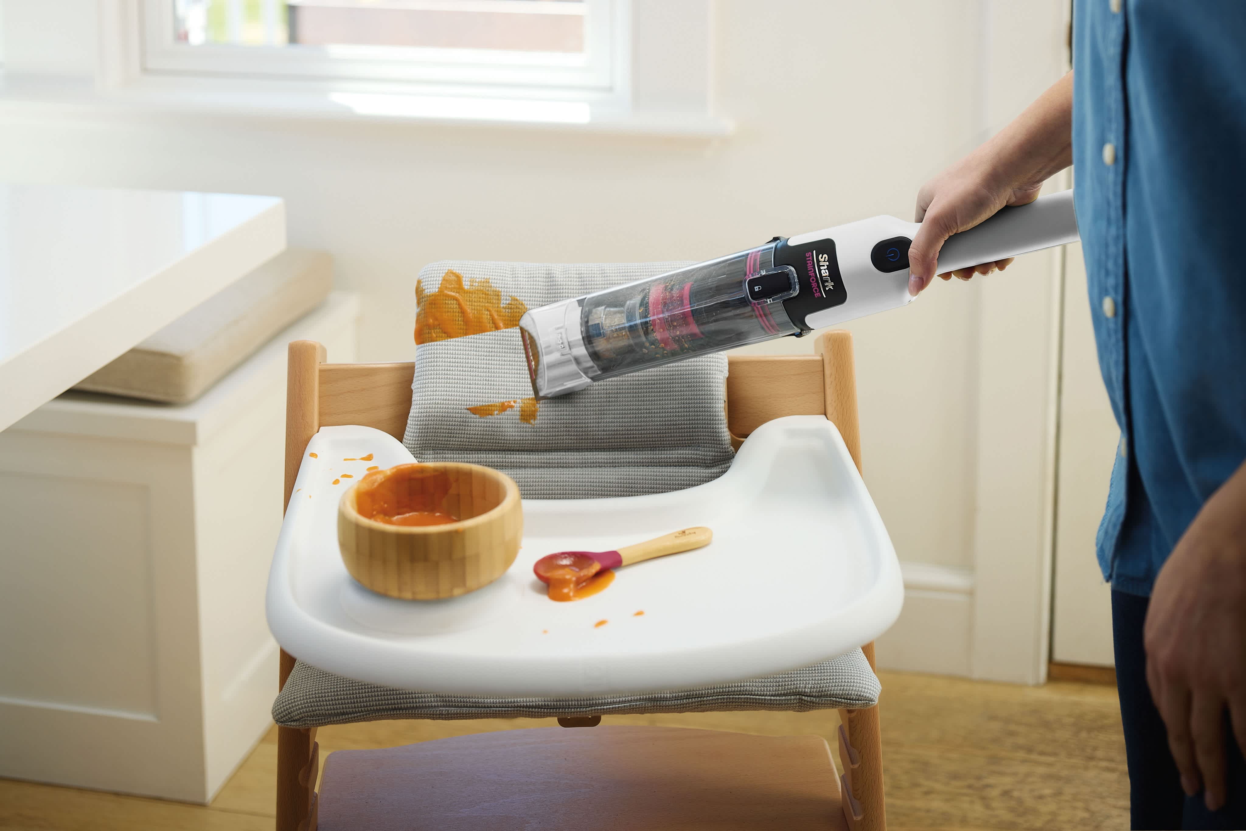 Person using a Shark StainForce cordless handheld to clean spilled baby food from a highchair tray and cushion
