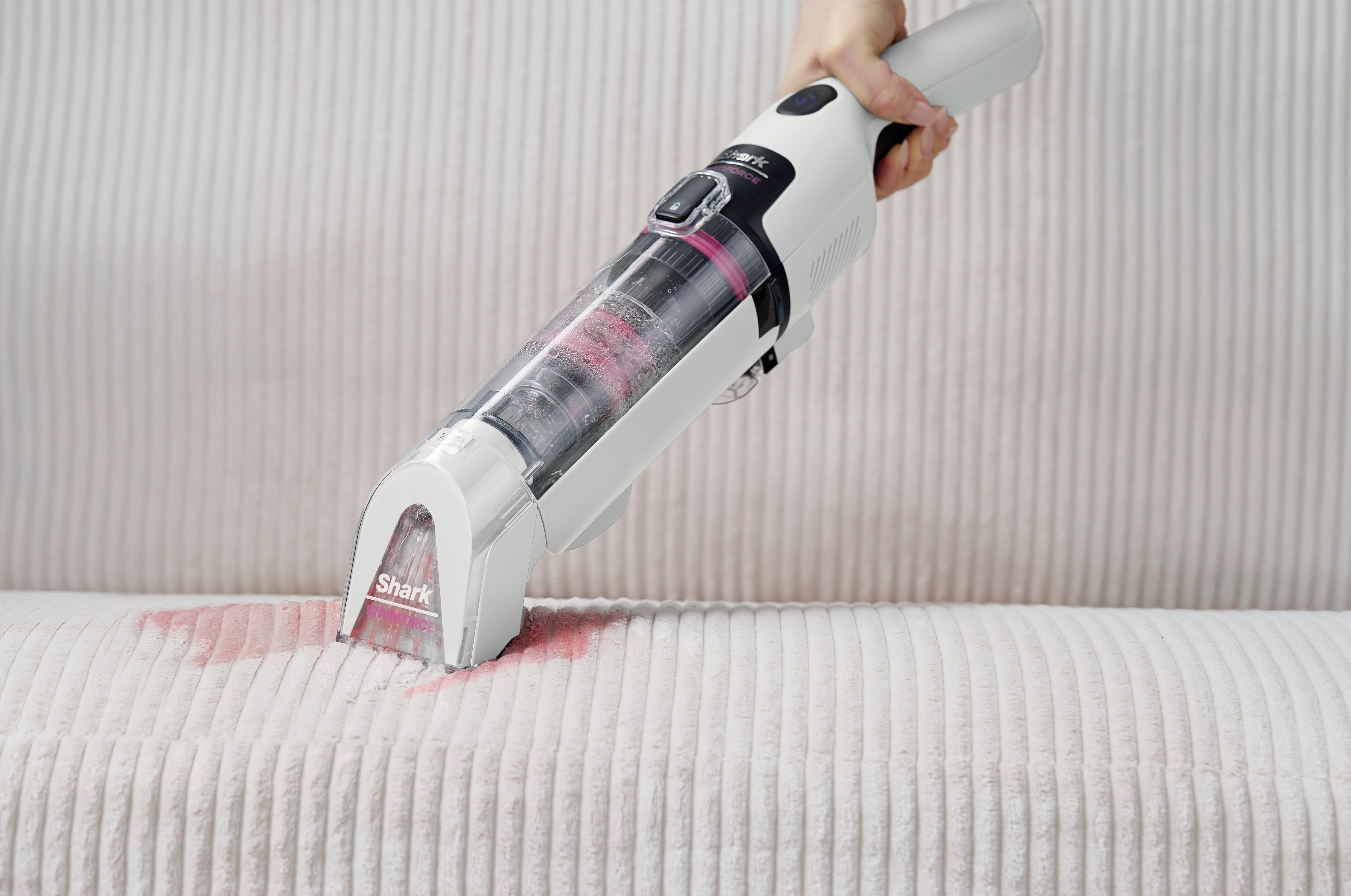 Person using a Shark StainForce Cordless handheld vacuum to clean red wine spilled on a light-coloured upholstery surface.