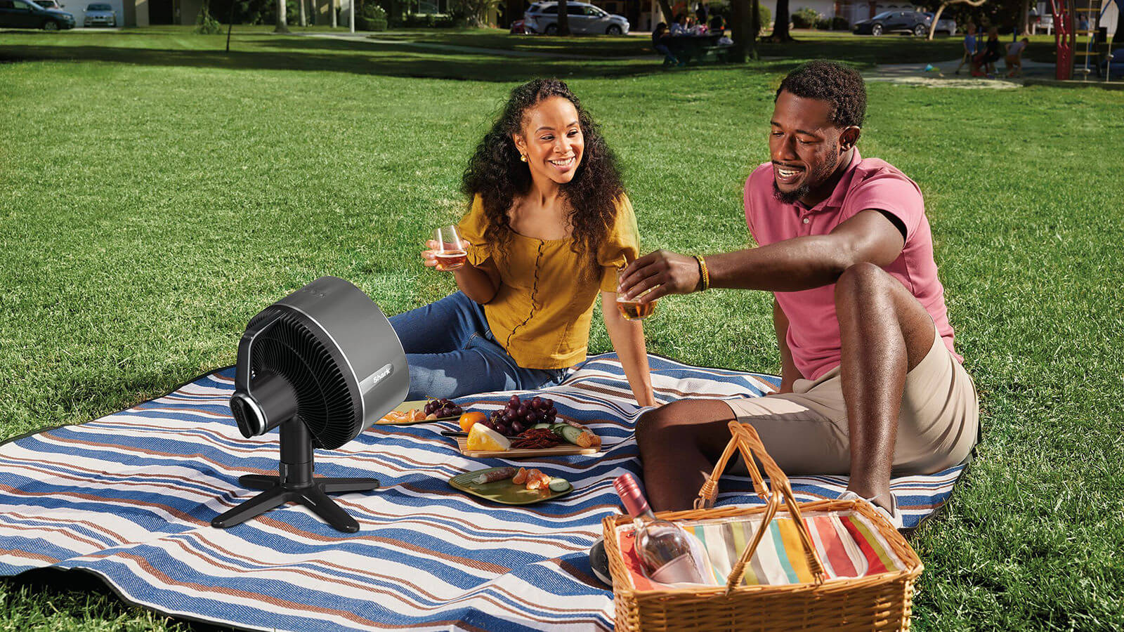 Image of Man and Woman sat outside having a picnic with the Shark Hydro Go Fan