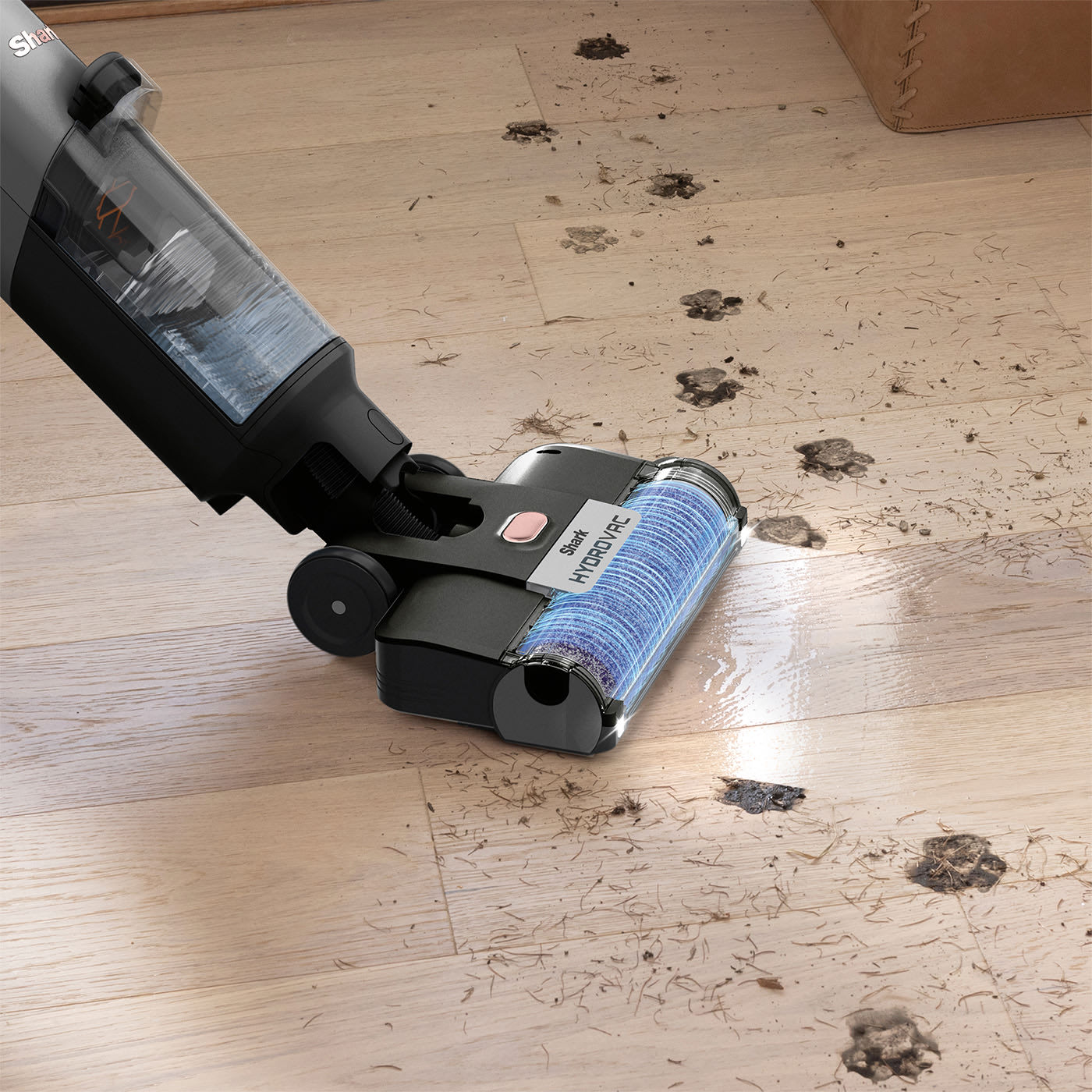 Close-up of a Shark wet/dry floor cleaner; the brush roll lifts muddy paw prints and pet hair from light wooden flooring.