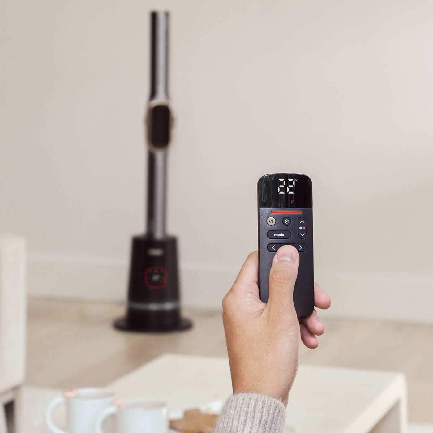 Close up of a hand holding a remote control with power,mode and directional buttons, pointed at the Shark Turbo Blade cool and heat fan